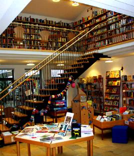 Innenansicht der Pfarrbücherei St. Hildegard München: Regale und Tisch mit Büchern und Treppe in den 1. Stock