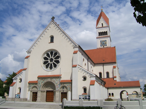 Westportal der Pfarrkirche Maria Schutz mit dem großen Rosettenfenster. Darunter die Eingangstüren, im Hintergrund der 66 Meter hohe Turm.