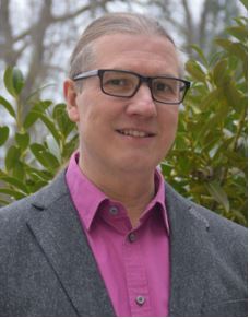 Bild des Diakons vor einer grünen Hecke