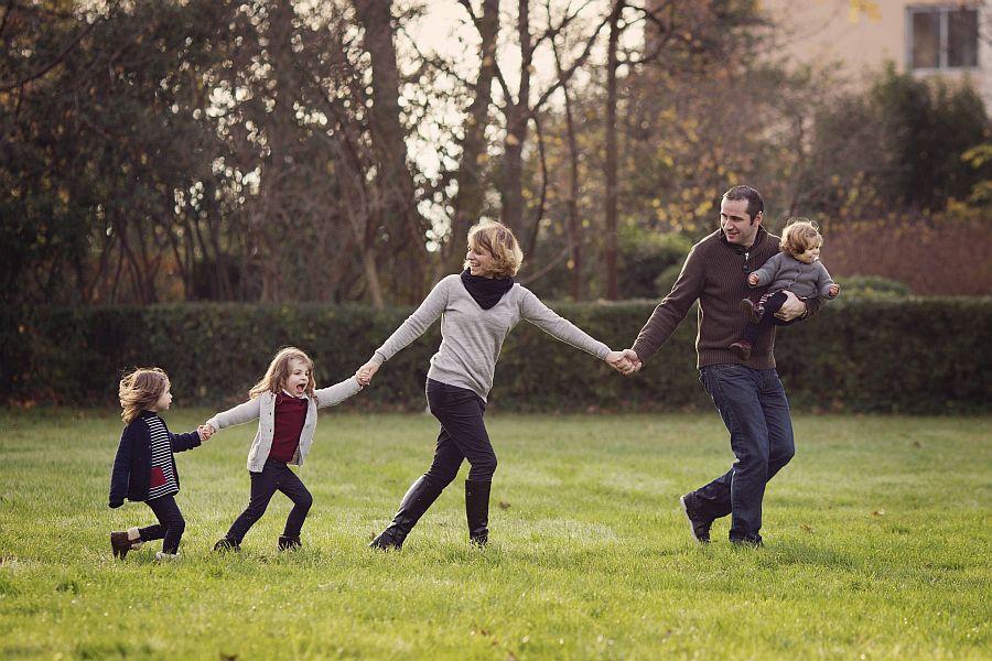 Eltern und drei Kinder laufen in Reihe über Wiese und halten sich an der Hand
