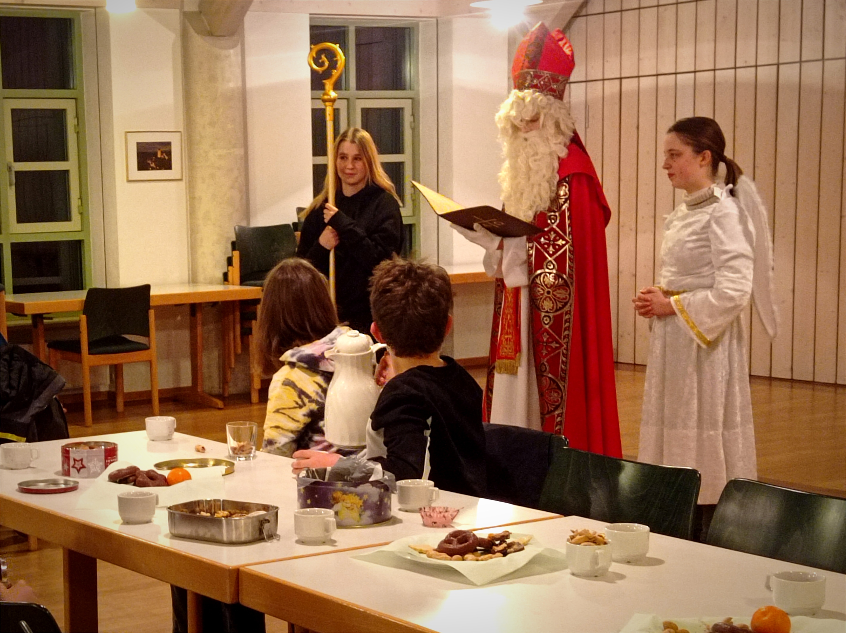 Der Nikolaus und ein Engel stehen vor der Ministrantenschar und berichten, was im vergangenen Jahr alles passiert ist