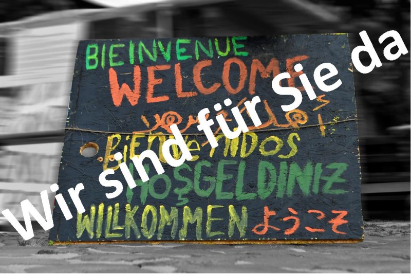 Schwarze Tafel auf der in bunten Kreidefarben Willkommen, Welcome, Bieinvenue, und schräg "Wir sind für Sie da" steht.