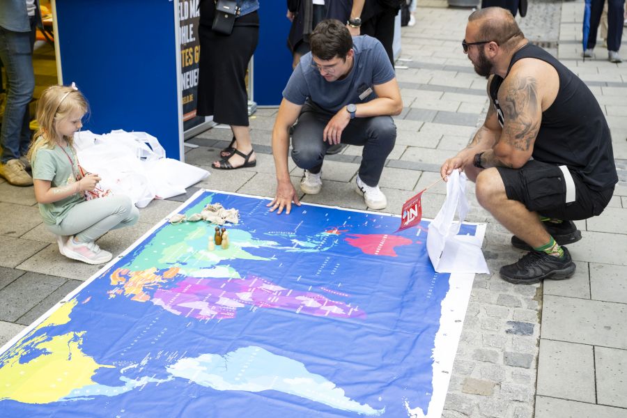 Kind und Erwachsener beugen sich über Weltkarte am Boden der Münchner Fußgängerzone beim Bennofest 2024