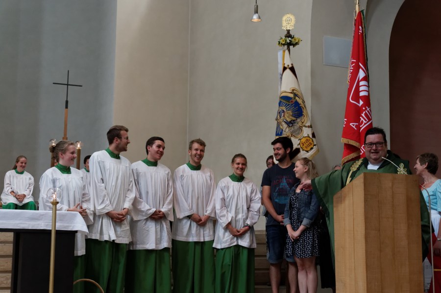 Ministranten stehen am Altar, daneben zwei Jugendliche. Man sieht auch eine Fahnenabordnung. Am Altar steht Martin Cambensy und zeigt lachend auf die Jugendlichen.