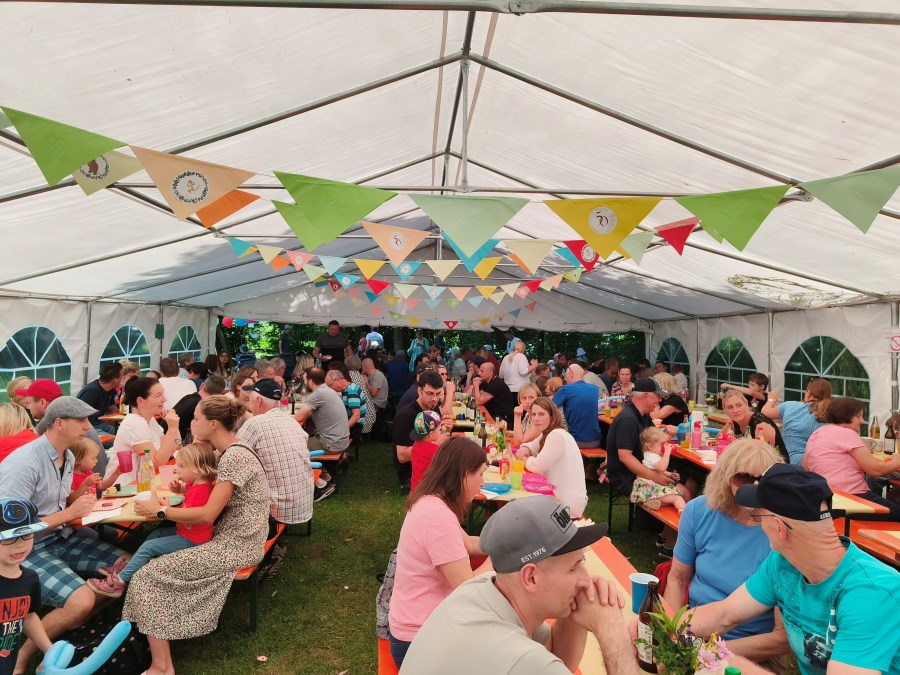 Zusammensein im schön dekorierten Zelt, Eltern und Kinder an Biertischgarnituren im Gespräch