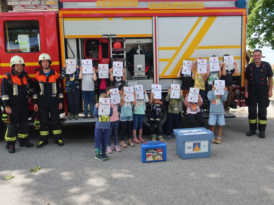 Die Kinder stehen vor dem Feuerwehrauto und halten ihre Urkunde vor ihre Gesichter