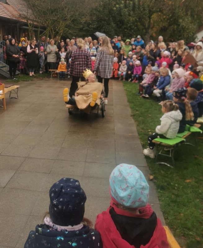 Der Kartoffelkönig hüpft in die Schubkarre der armen Kinder. Die Mitarbeiterinnen des Kinderhauses führen die "Geschichte vom Kartoffelkönig" für die Kinder auf.