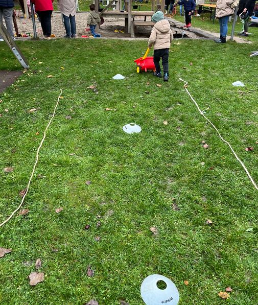 ein Kind schiebt eine Schubkarre mit einem Kürbis über die Wiese.