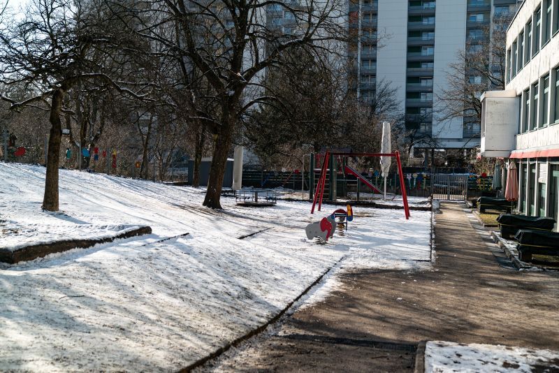 Große, verschneite Freispielfläche mit Klettergerüst der KiTa St. Lukas inmitten von Hochhäusern