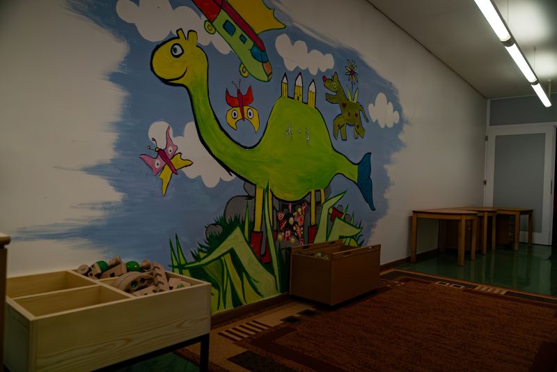 Wandgemälde: Grüner Dinosaurier mit Schmetterlingen und einem Flugzeug