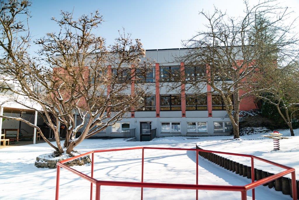 Außenansicht des roten Kinderhauses Maria Schutz vom verschneiten Garten aus.