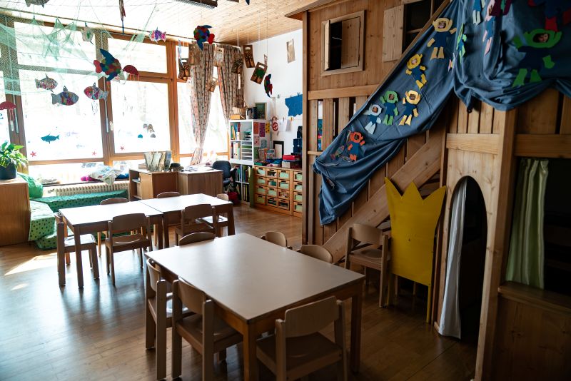 Gruppenraum mit Tischen und Stühlen und einem hölzernen Spielhaus in der Kita St. Hildegard.