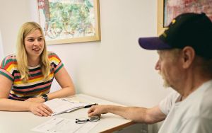 Beratung eines älteren Herrn durch eine junge Mitarbeiterin am Schreibtisch beim Katholischen Männerfürsorgeverein München