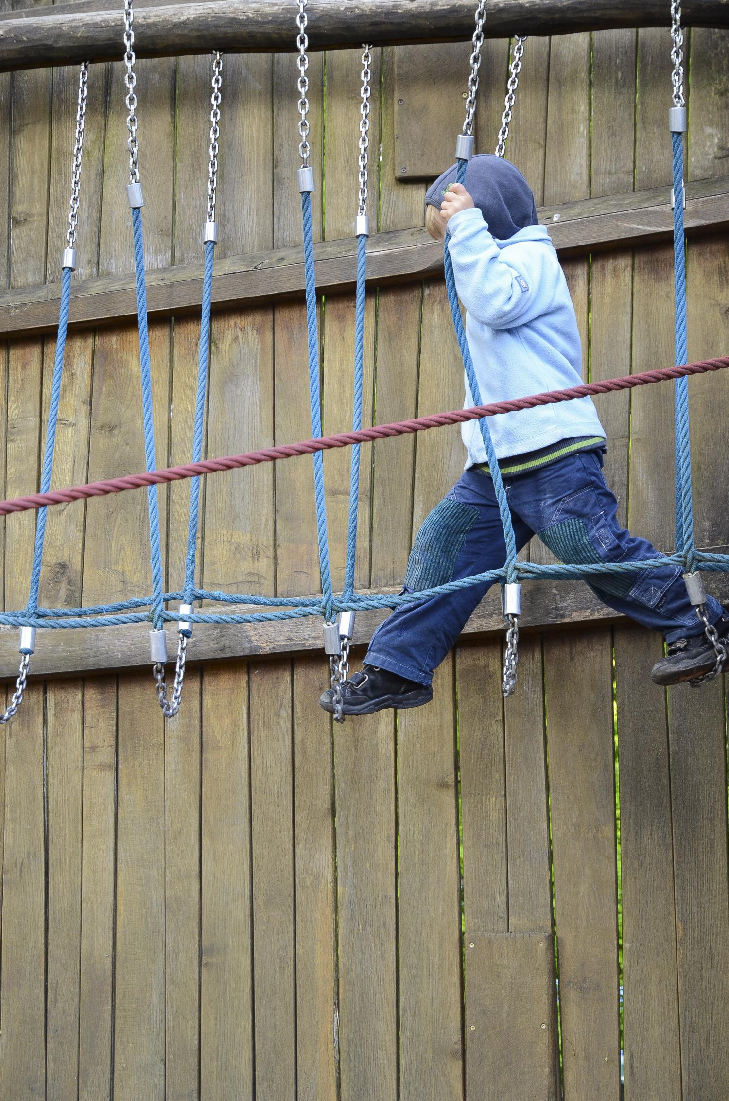 Kind macht große Schritte in luftiger Höhe eines Klettergerüstes aus Tauen und Ketten