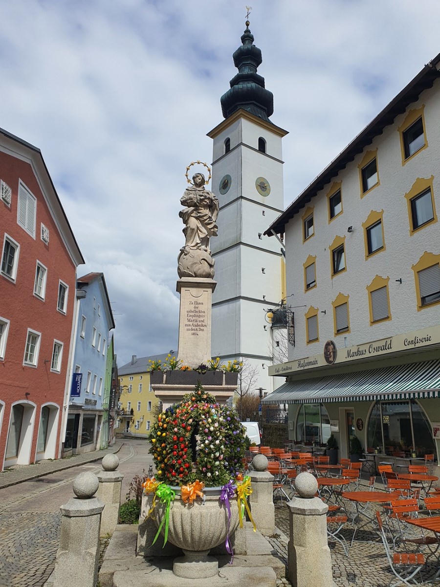 Der Osterbrunnen in Waging an der Mariensäule. Dahinter die Pfarrkirche St. Martin in Waging