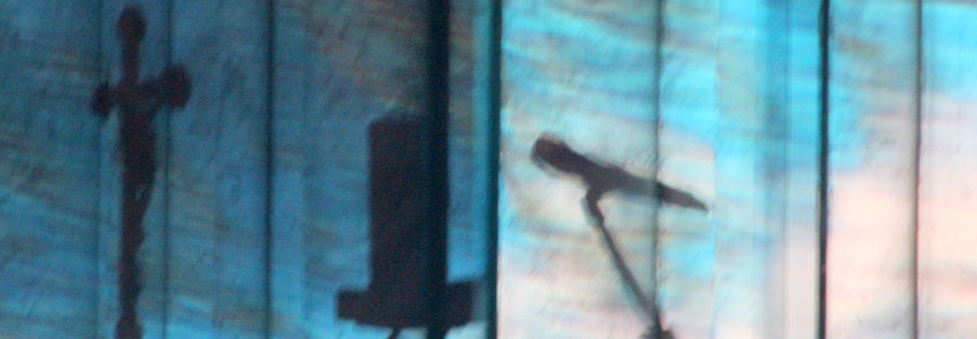 Schatten eines Mikrofons und Kreuzes vor blau beleuchtetem Vorhang