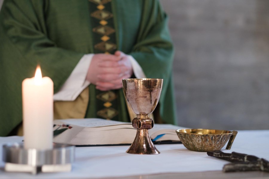 Priester in grünem Messgewand und Stola vor Kelch, Hostienschalte Kerze und Messbuch auf Altar