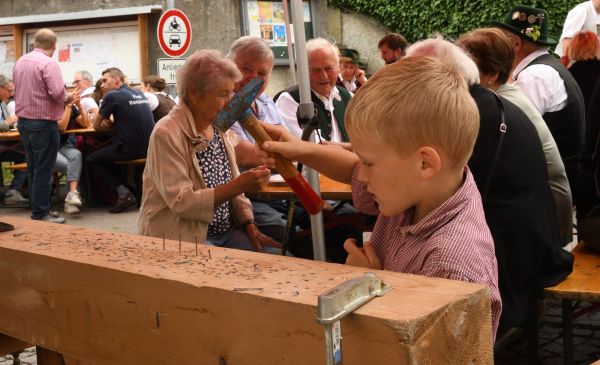 Kind beim Balkennageln, Gäste schauen im Hintergrund zu.