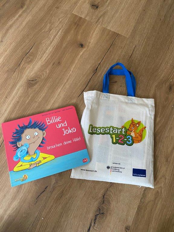 Buch "Billie und Jolo" und eine Tasche mit Aufschrift "Lesestart 123" liegen auf einem Tisch